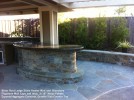 Bitter Root Ledge Stone Veneer Wall and Bluestone Flagstone Wall Caps and Inlay. 3_16” Noiyo Pebble Exposed Aggregate Concrete. Granite Slab Counter Top